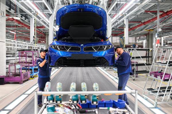 Deux opérateurs BMW travaillent sur la face avant d'une BMW i3 bleue au poste d'assemblage de l'usine de Munich