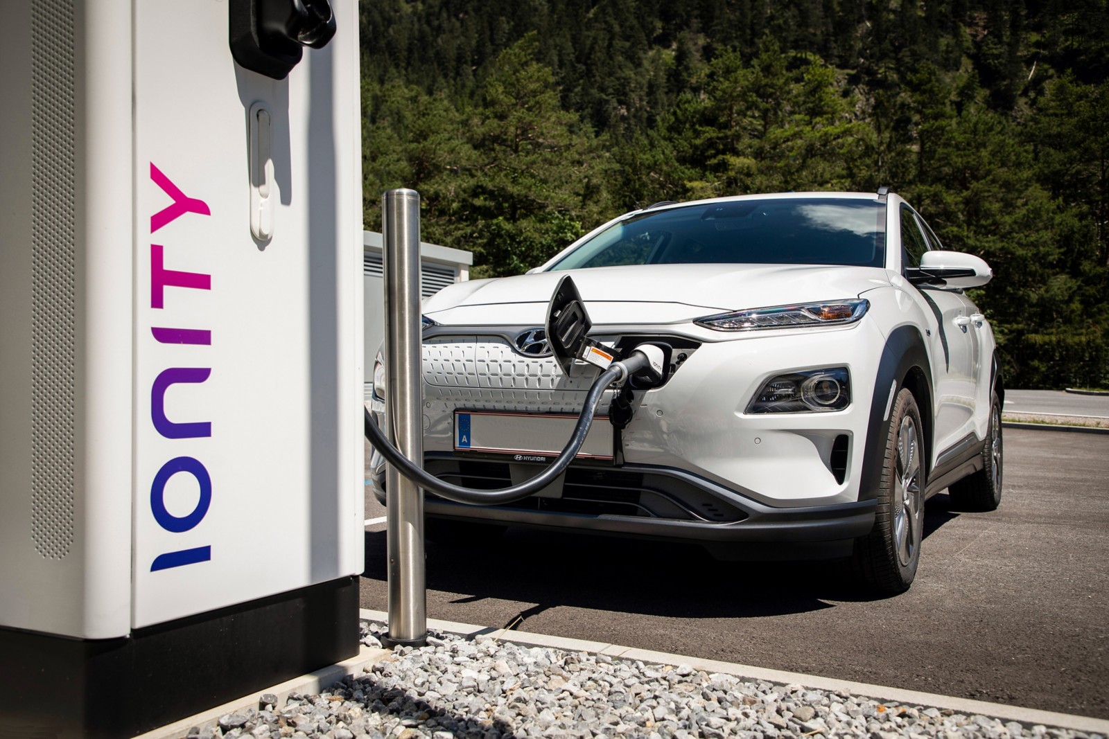 Connecteur de recharge rapide branché sur la prise avant d'un Hyundai Kona Electric blanc à une borne extérieure