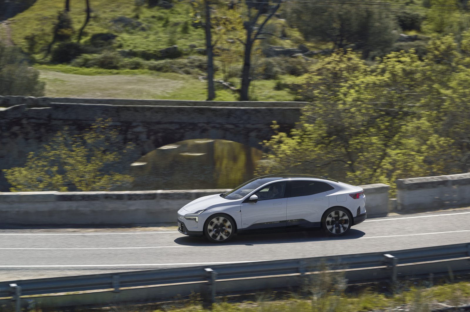 Polestar 4 grise circulant sur une route de campagne bordée d'un pont en pierre