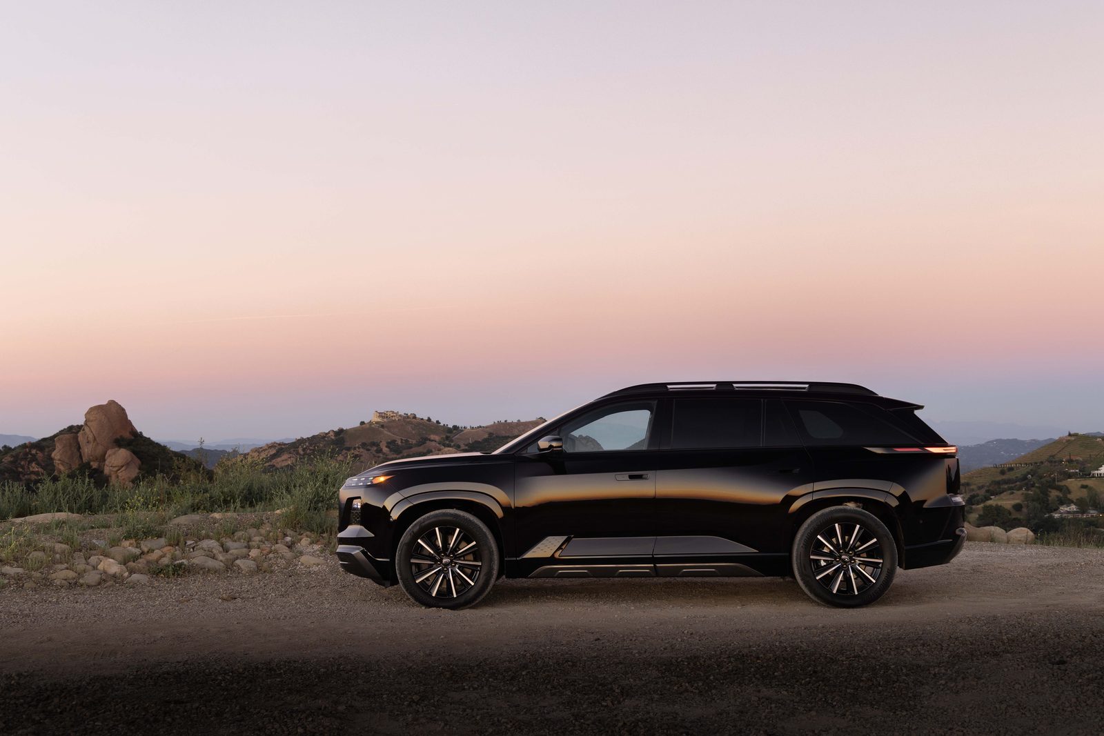 Profil du Subaru Getaway électrique noir arrêté sur un chemin de terre au coucher du soleil