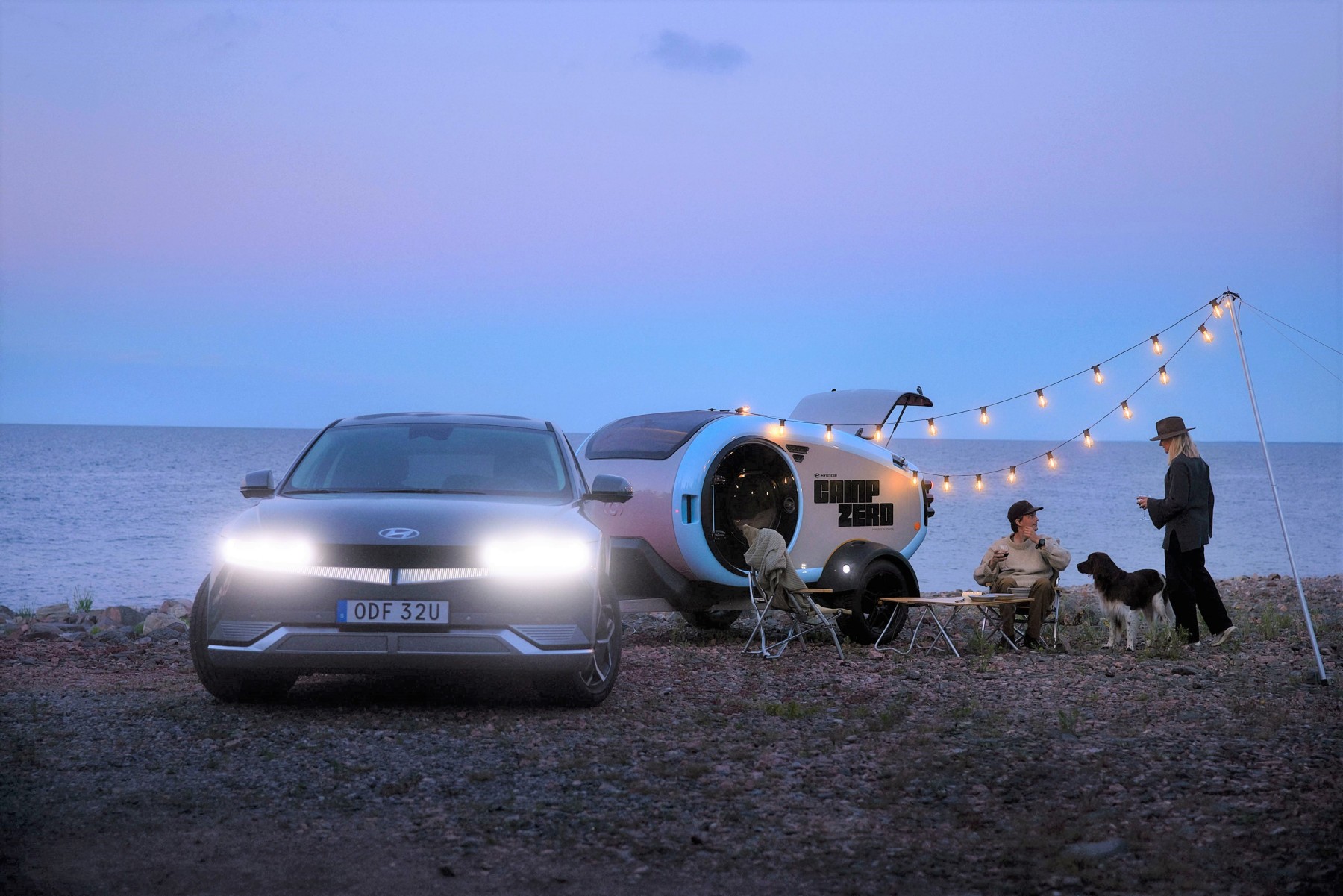 Hyundai IONIQ 5 attelée à une remorque de camping en bord de mer, phares allumés, à la tombée du jour