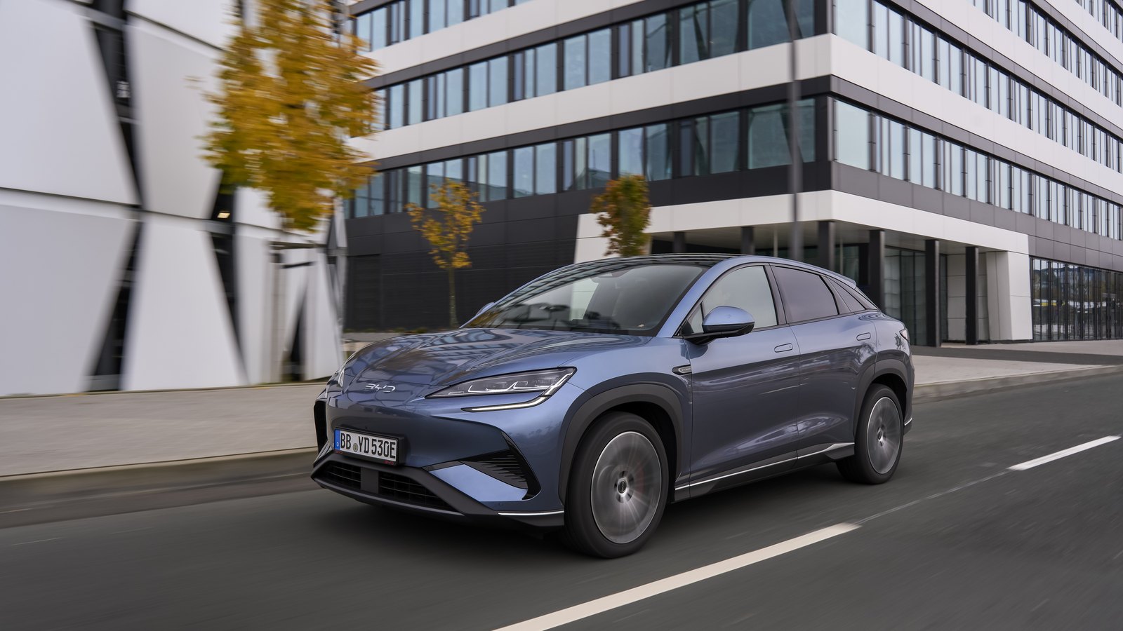 SUV électrique BYD Sealion 7 gris en roulage devant un immeuble de bureaux en Europe
