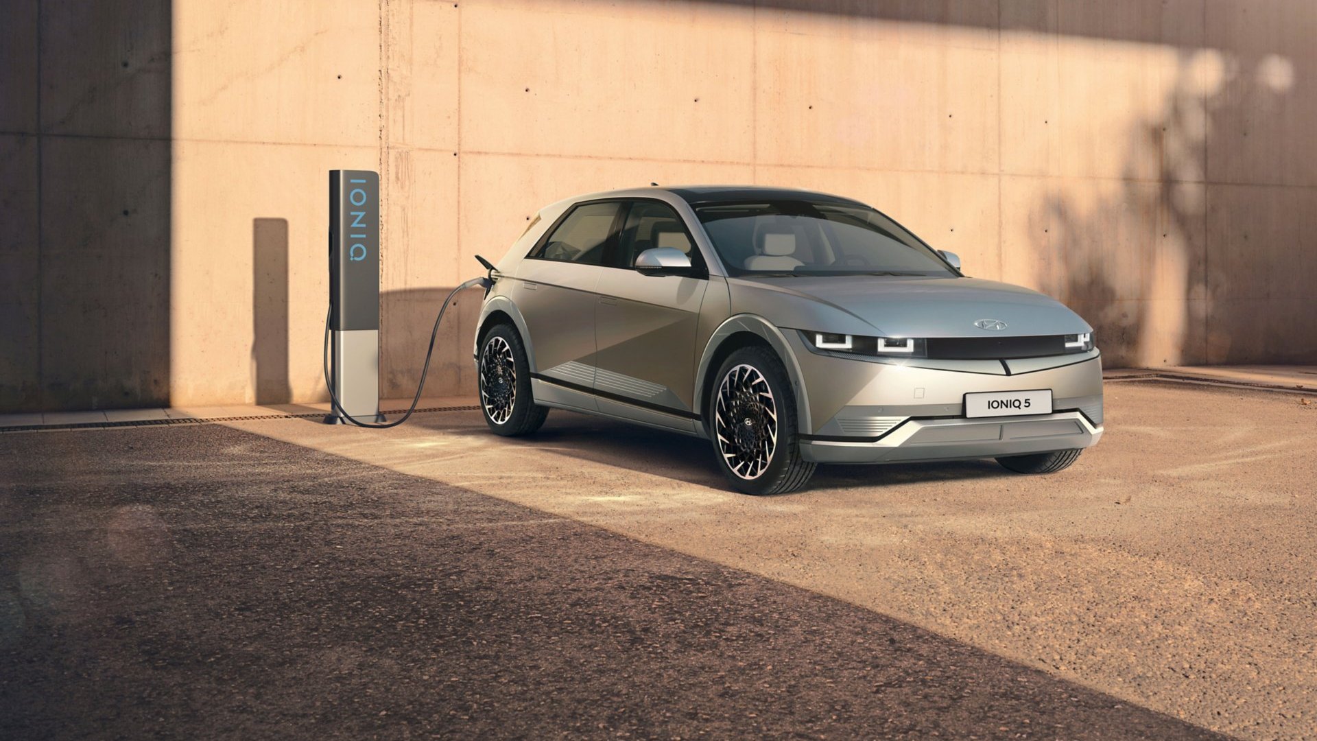 Hyundai IONIQ 5 grise branchée à une borne de recharge IONIQ devant un mur en béton