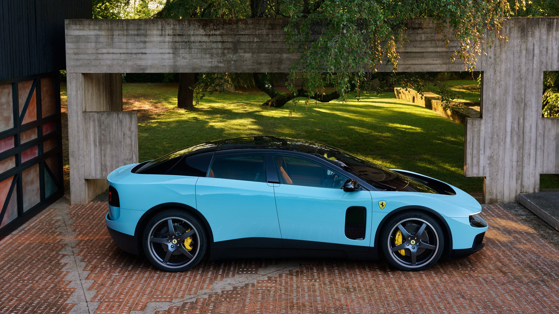 Ferrari Luce bleu clair vue de profil devant un bâtiment en béton, carrosserie quatre portes et jantes claires