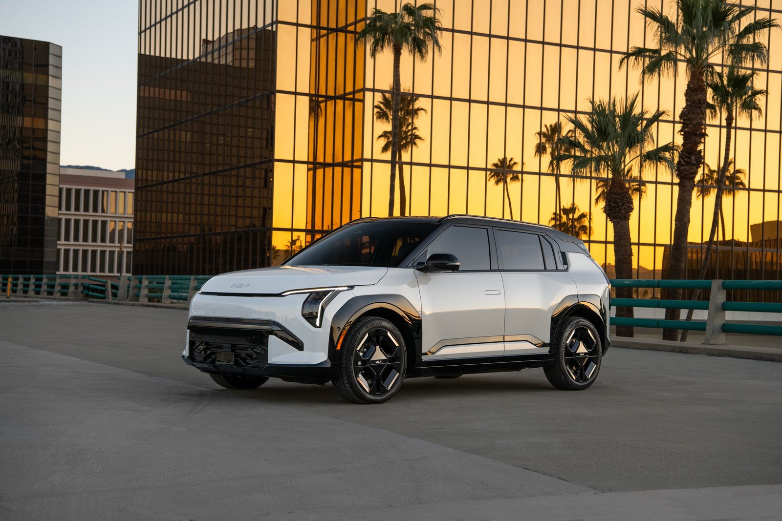 Kia EV3 blanc de trois quarts avant à l’arrêt devant un bâtiment vitré