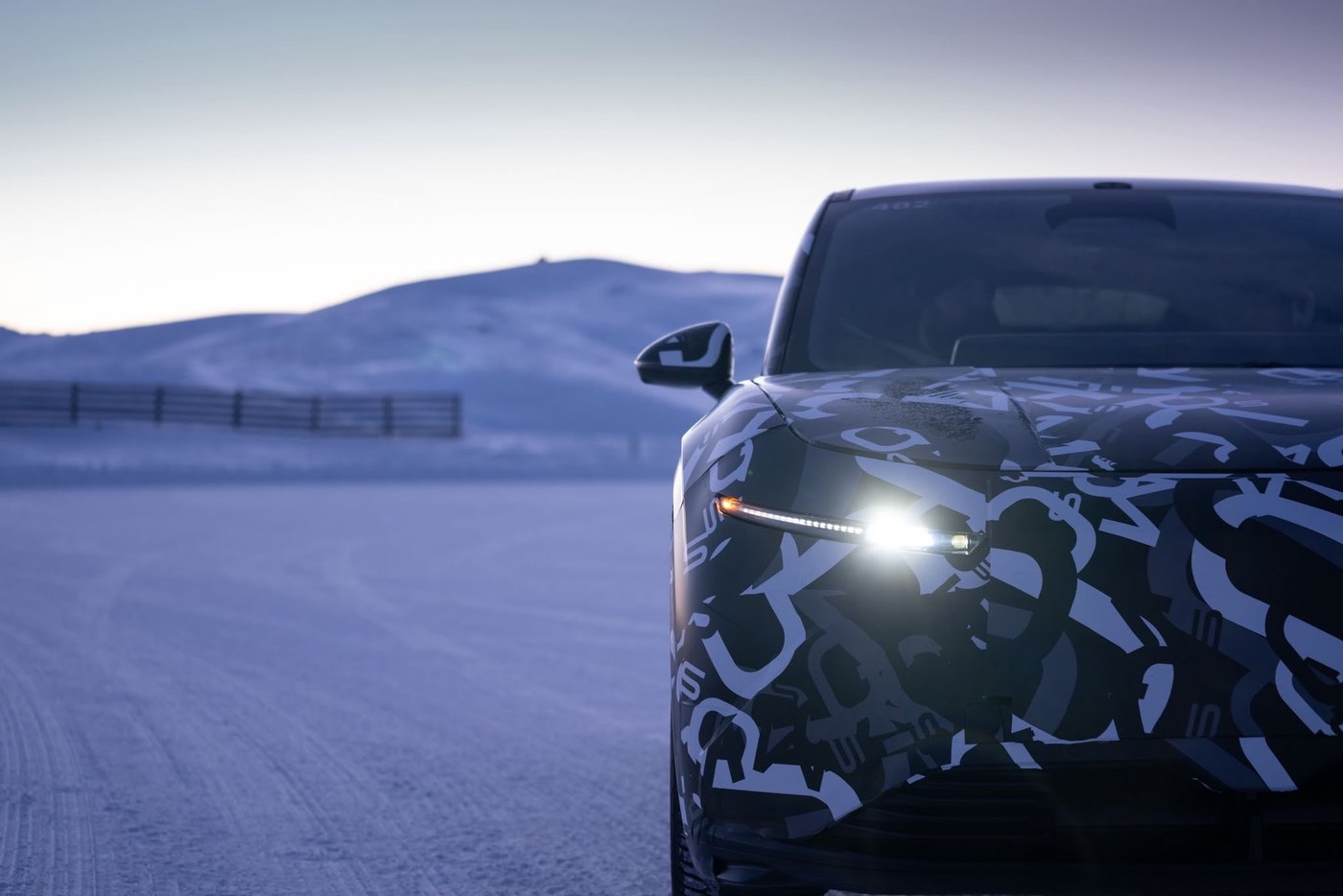Face avant du prototype Lucid Cosmos camouflé, phares allumés, à l'arrêt sur une piste enneigée au crépuscule