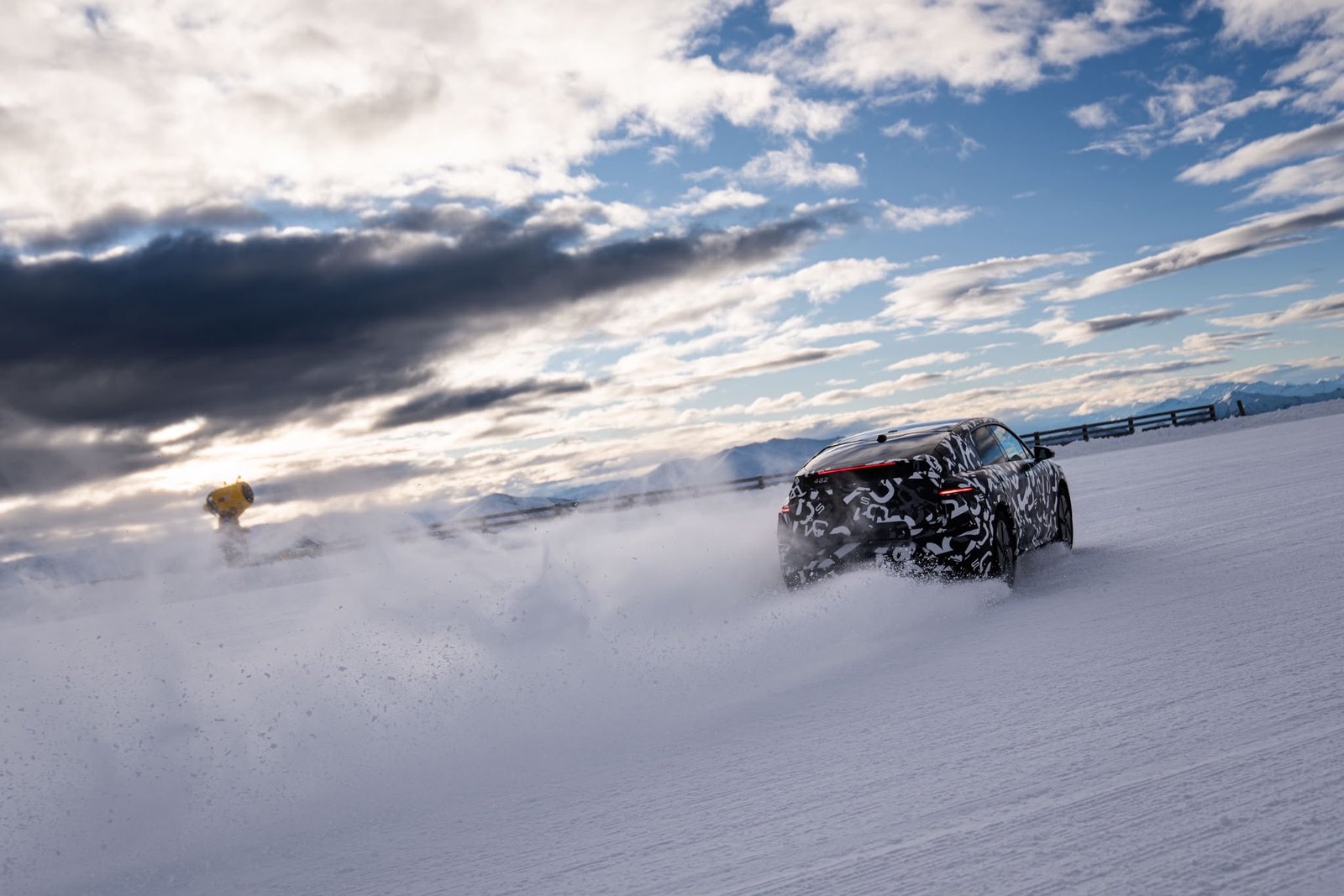 Prototype Lucid Cosmos camouflé en essais dynamiques sur une piste enneigée de Nouvelle-Zélande, projetant un nuage de neige