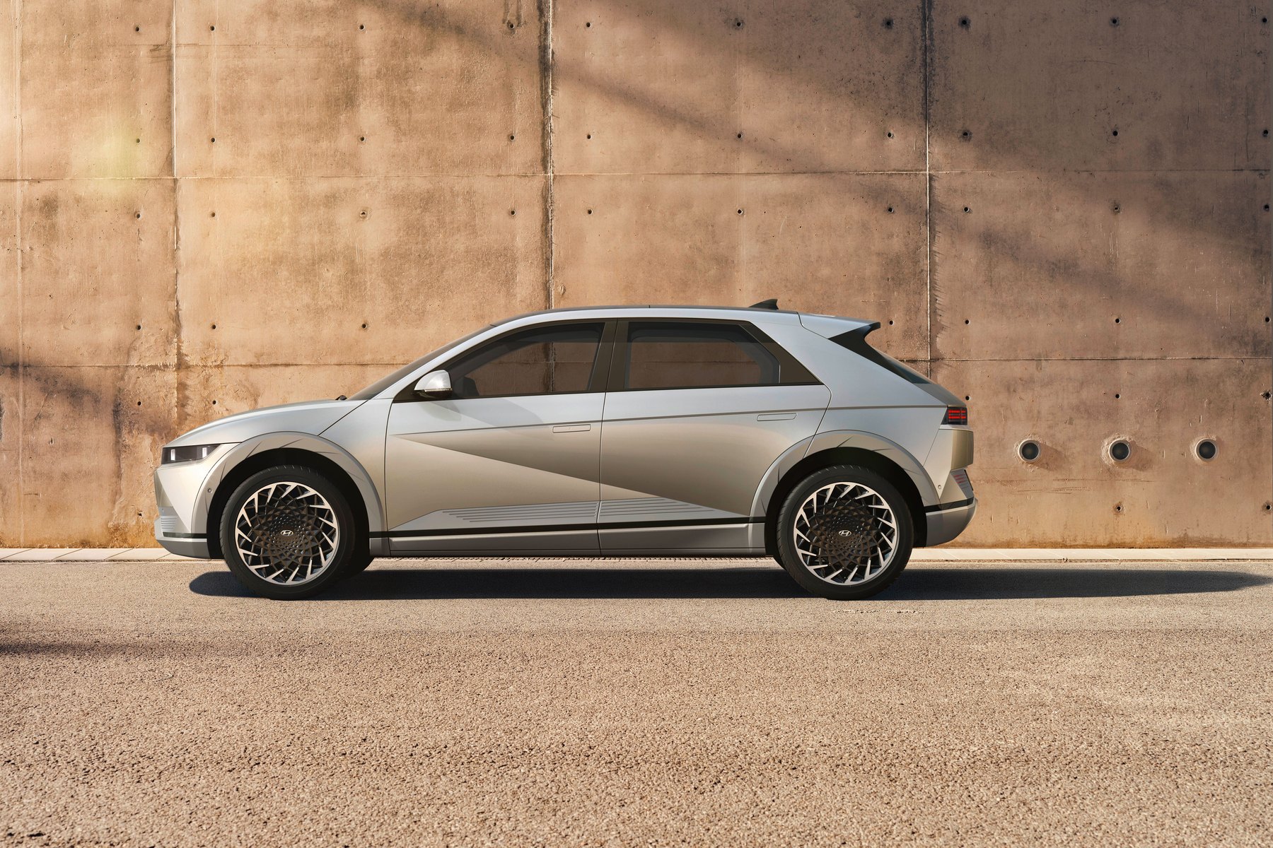 Hyundai IONIQ 5 grise vue de profil devant un mur de béton, ses quatre roues au sol