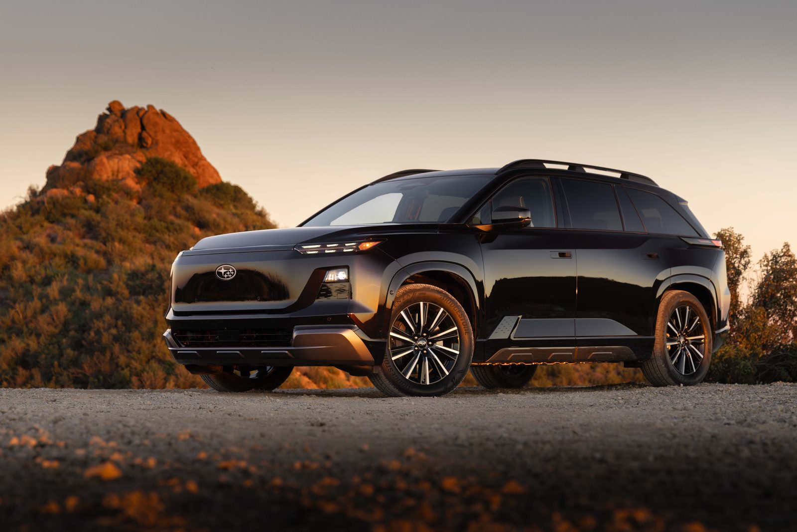 Subaru Getaway électrique noir vu de trois quarts avant sur un chemin de terre, phares allumés, au coucher du soleil
