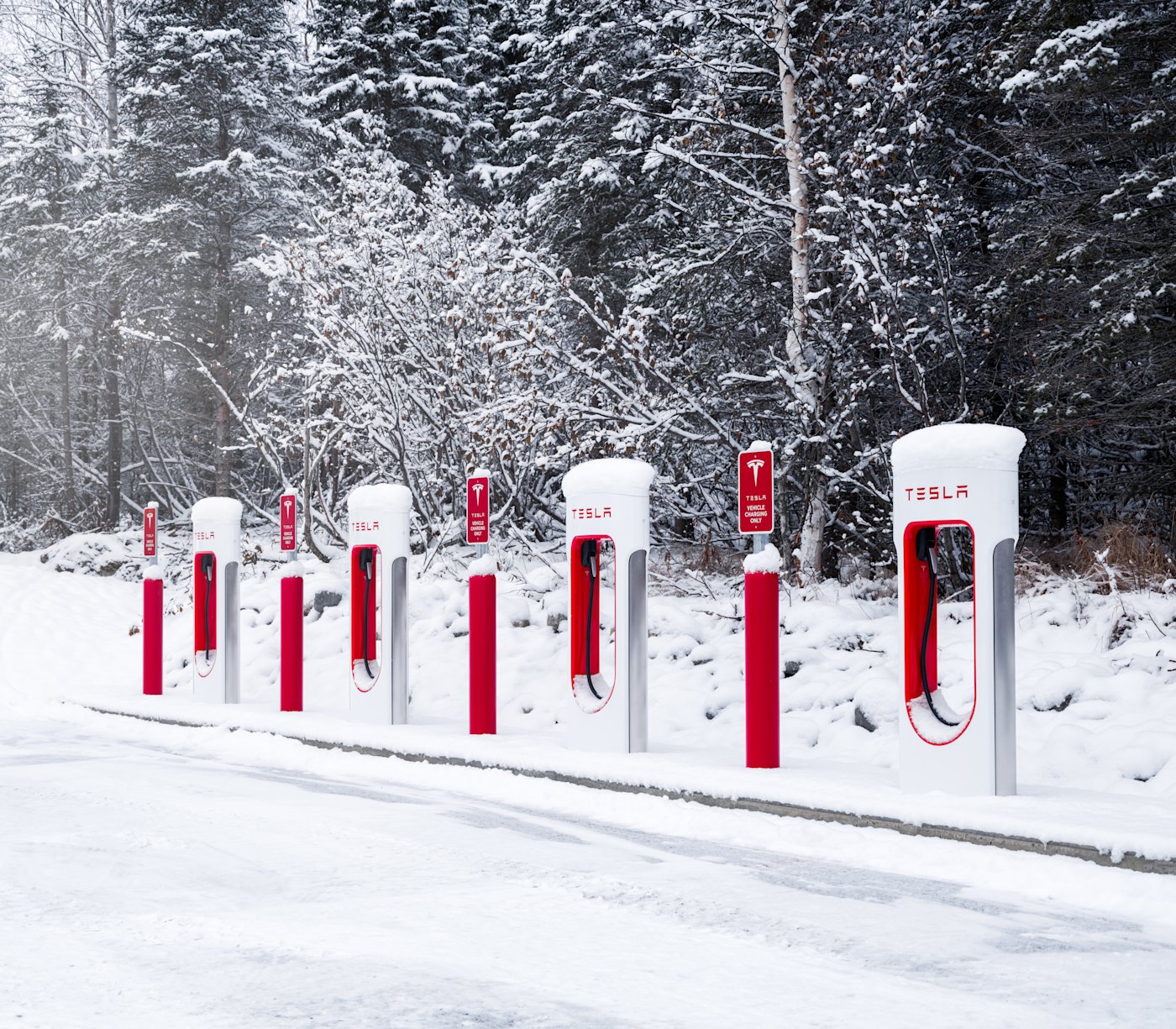 Berline Tesla branchée à un Superchargeur en station, prise de recharge visible sur le côté du véhicule