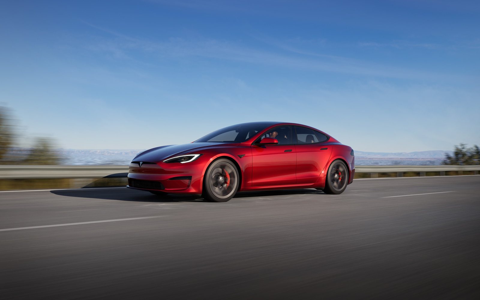 Tesla Model S rouge sur route ensoleillée sous un ciel dégagé
