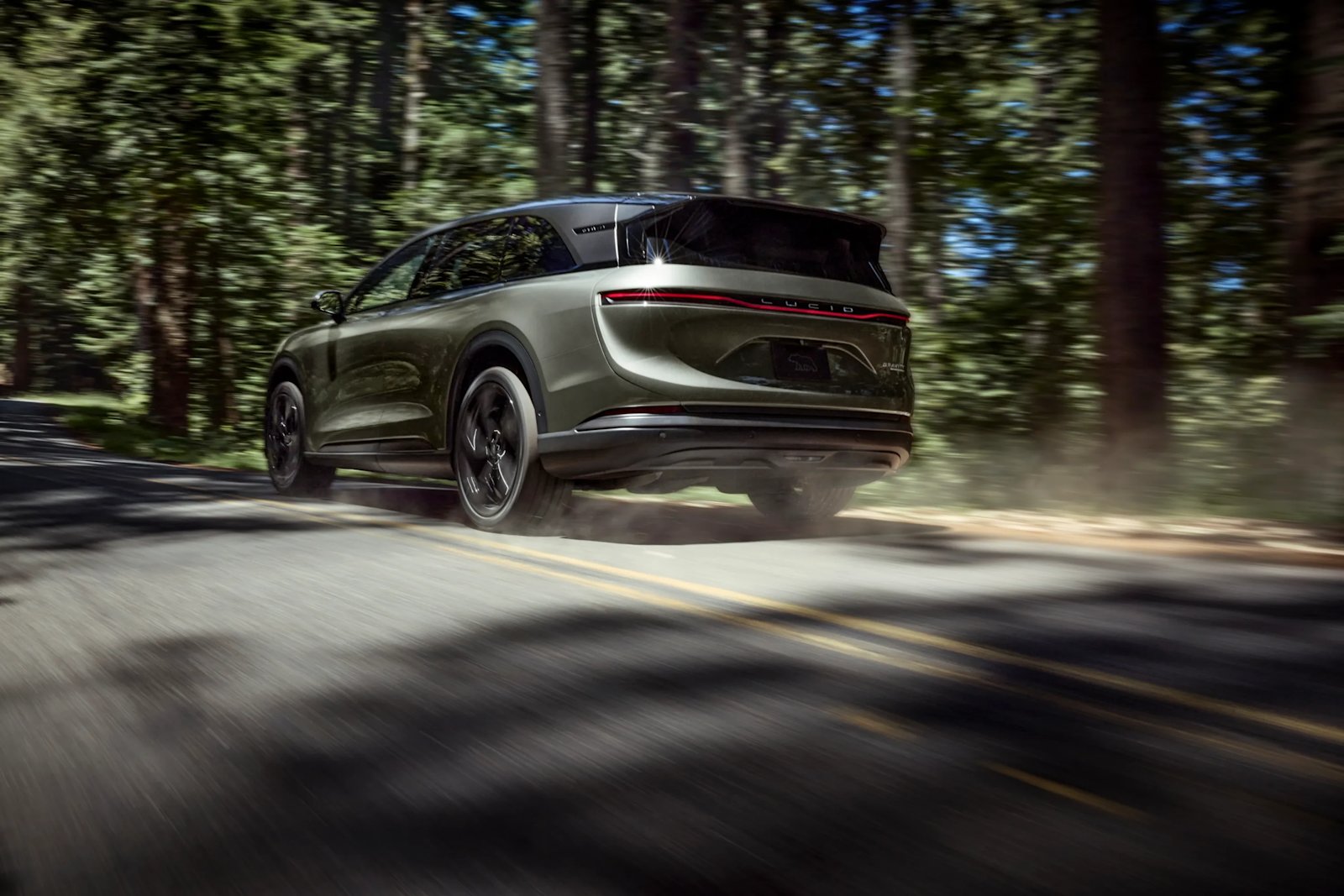 Lucid Gravity vert de trois quarts arrière en mouvement sur une route de forêt