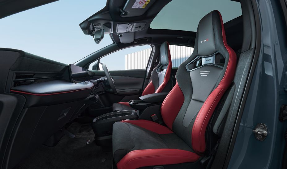 Habitacle avant de la Nissan Leaf NISMO vu depuis le côté conducteur : sièges baquets sport noir et rouge, ambiance sombre à surpiqûres rouges
