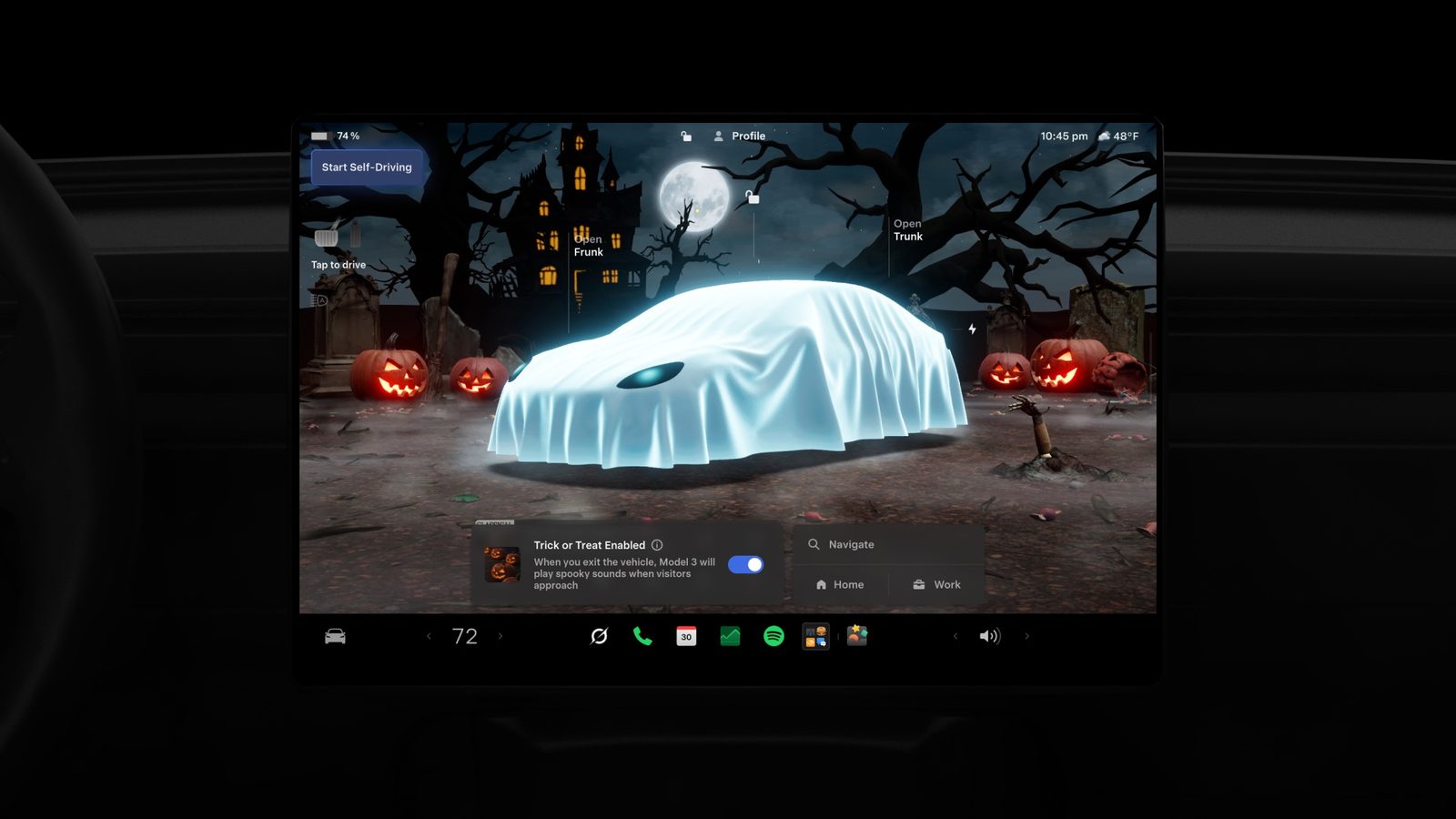 Écran central Tesla en mode Halloween : avatar du véhicule recouvert d'un drap de fantôme dans un décor de cimetière avec citrouilles