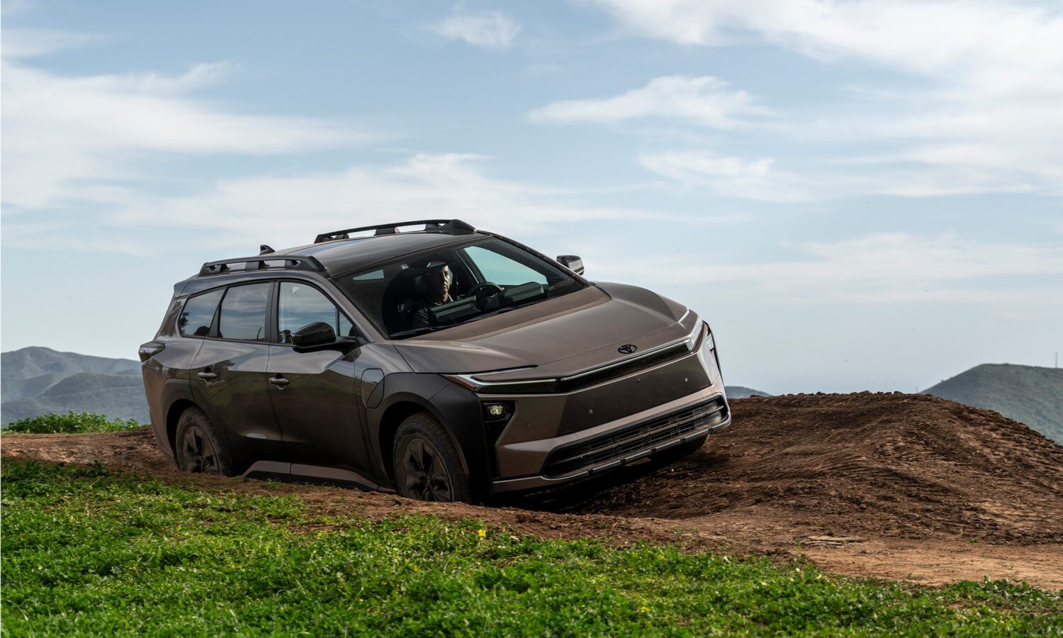 Toyota bZ Woodland 2027 de couleur bronze franchissant un talus de terre en pleine nature, vue de trois quarts avant