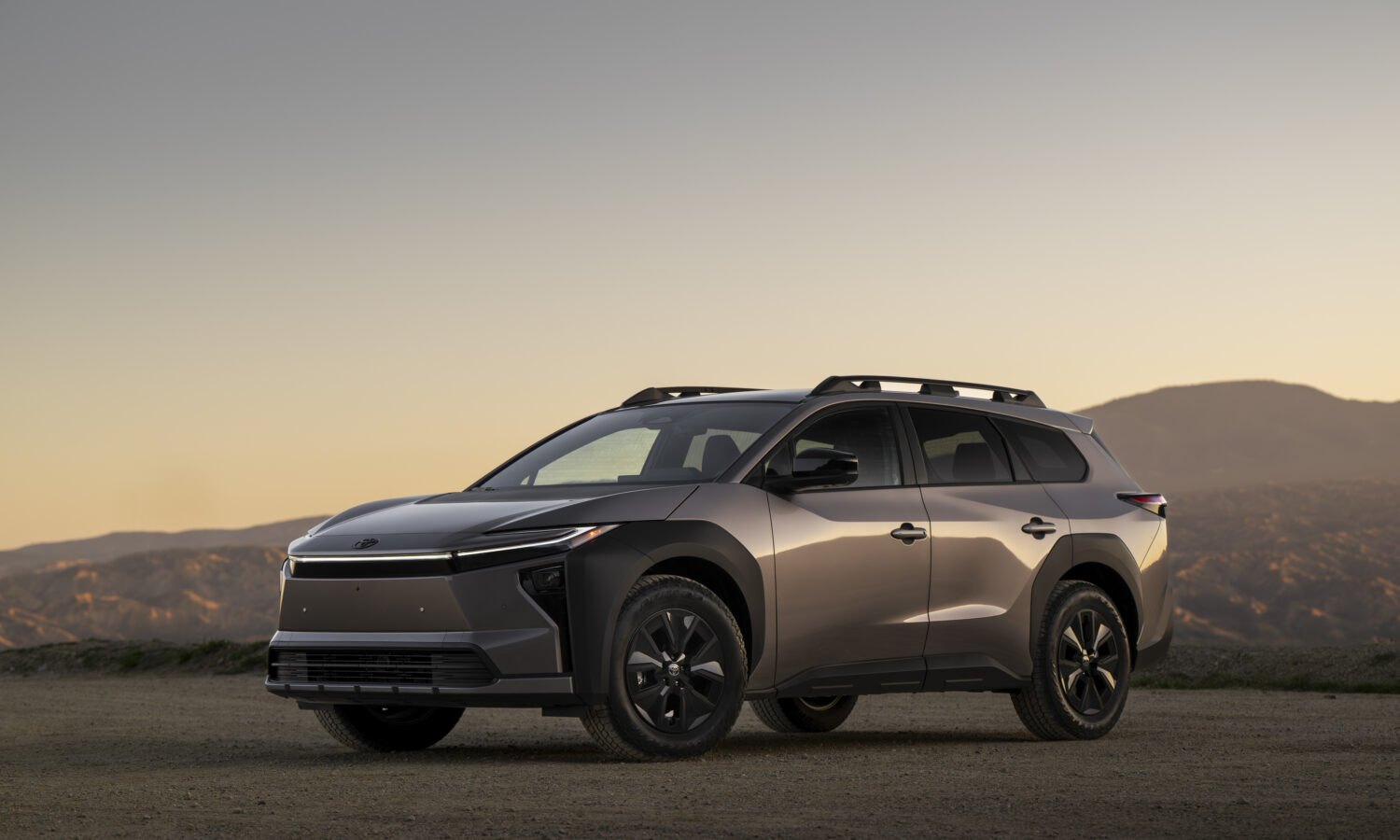 Toyota bZ Woodland 2027 de profil trois quarts avant, arrêté sur une piste de terre au crépuscule devant des collines